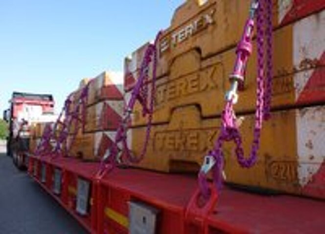 Schwere TEREX-Gewichte auf einem Tieflader mit pinken RUD-Zurrketten gesichert.