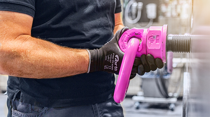 Montage eines pinken RUD-Anschlagpunkts durch eine Person mit Arbeitshandschuhen in industrieller Umgebung.