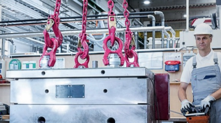 Schwere Metalllast wird in Produktionshalle mit RUD-Anschlagpunkten und Kettengehängen von Fachkraft sicher gehoben.