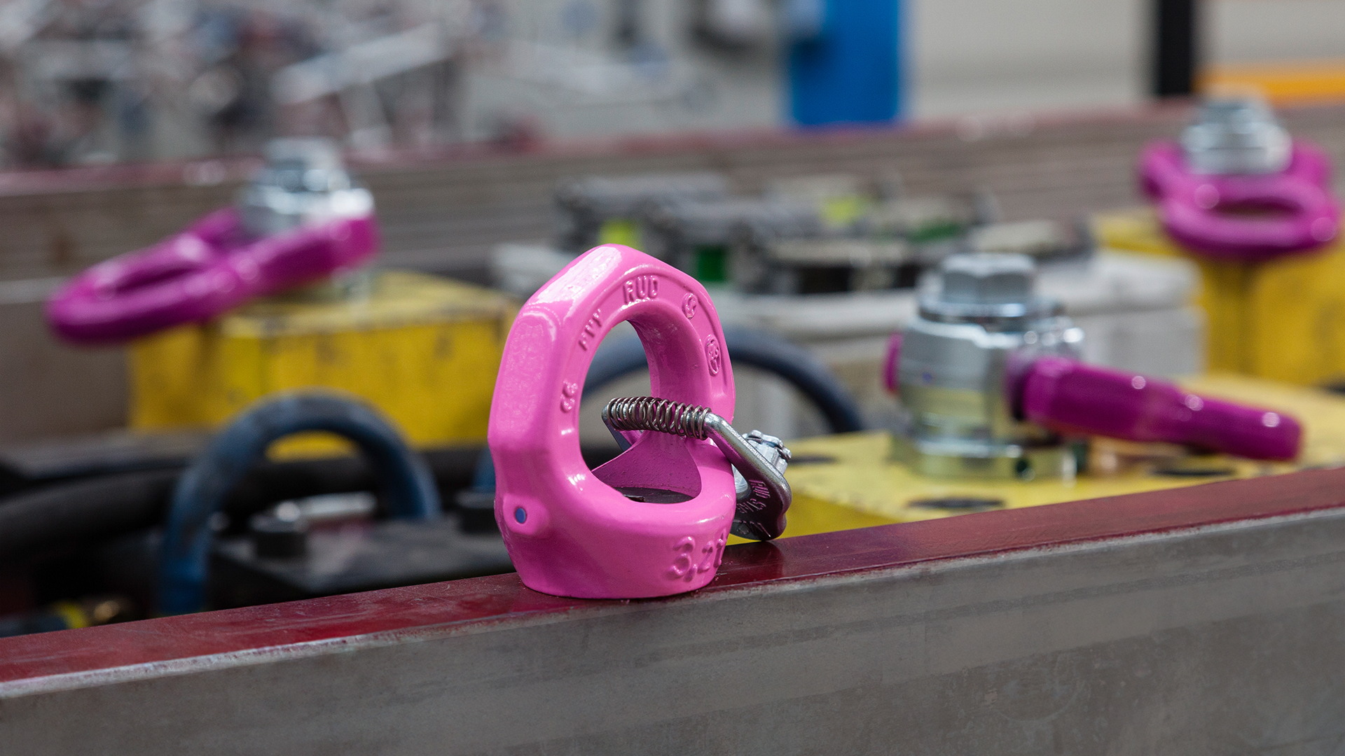 Nahaufnahme eines pinken RUD-Anschlagpunkts in einer Industrieumgebung mit weiteren Beschlägen im Hintergrund.