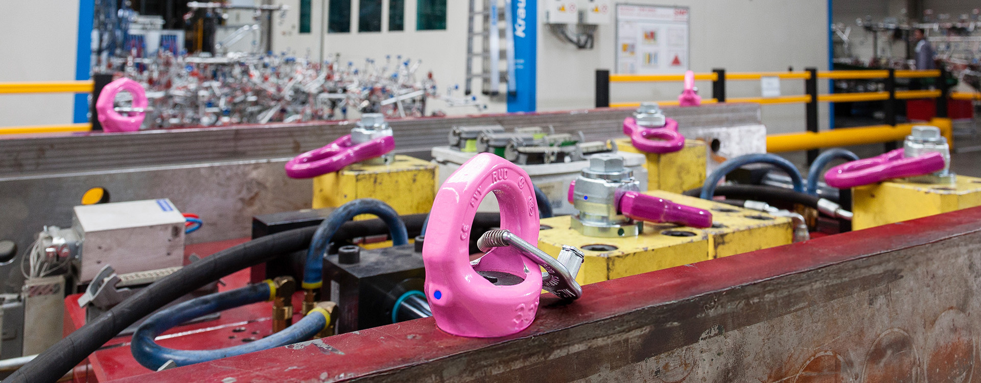 RUD-Anschlagpunkte in Pink montiert auf gelben Vorrichtungen in einer Industriehalle mit Maschinen.