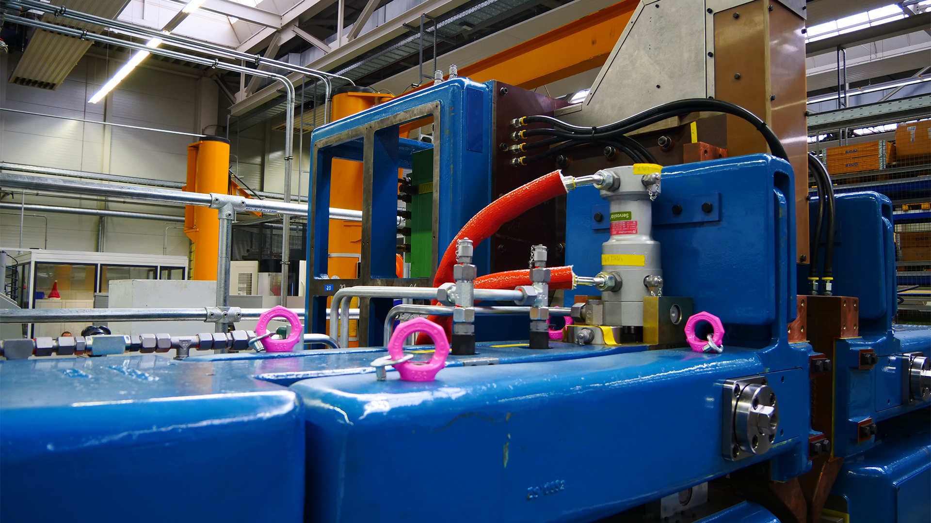 Industrielle Fertigungsanlage mit Hydrauliksystemen und farblich markierten Sicherheitsvorrichtungen.