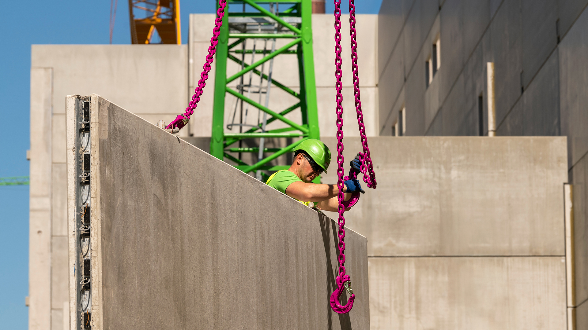 Bauarbeiter hebt eine Betonelementwand mit pinkfarbenen Ketten in einer Baustellenumgebung.