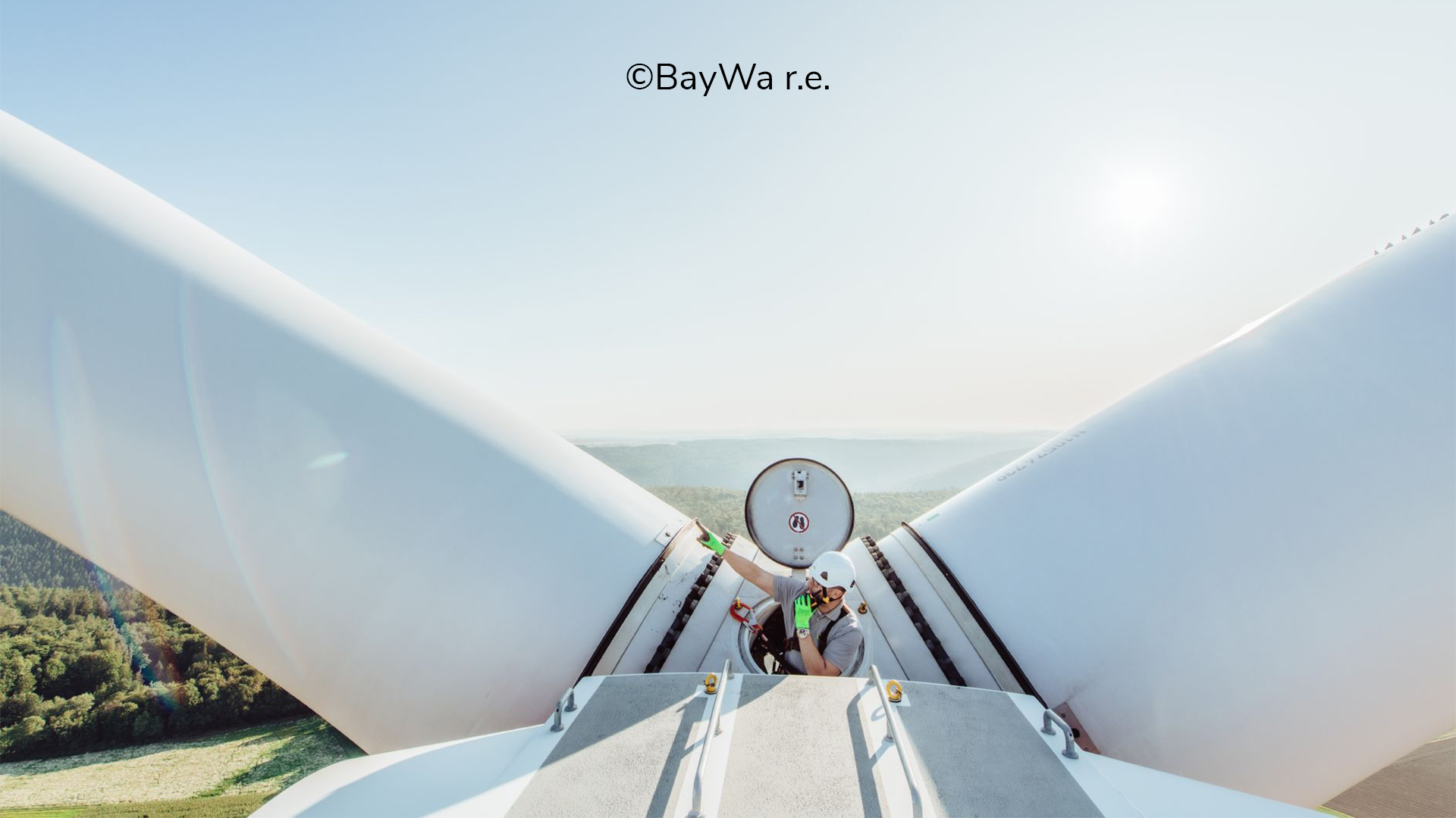 Techniker arbeitet auf der Spitze eines Windkraftwerks, Blick auf die Rotorblätter und die umliegende Landschaft.