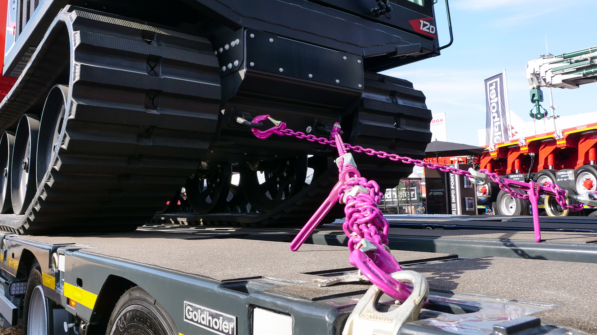 Schweres Fahrzeug auf einem Transportanhänger, gesichert mit pinkfarbenen Ketten.