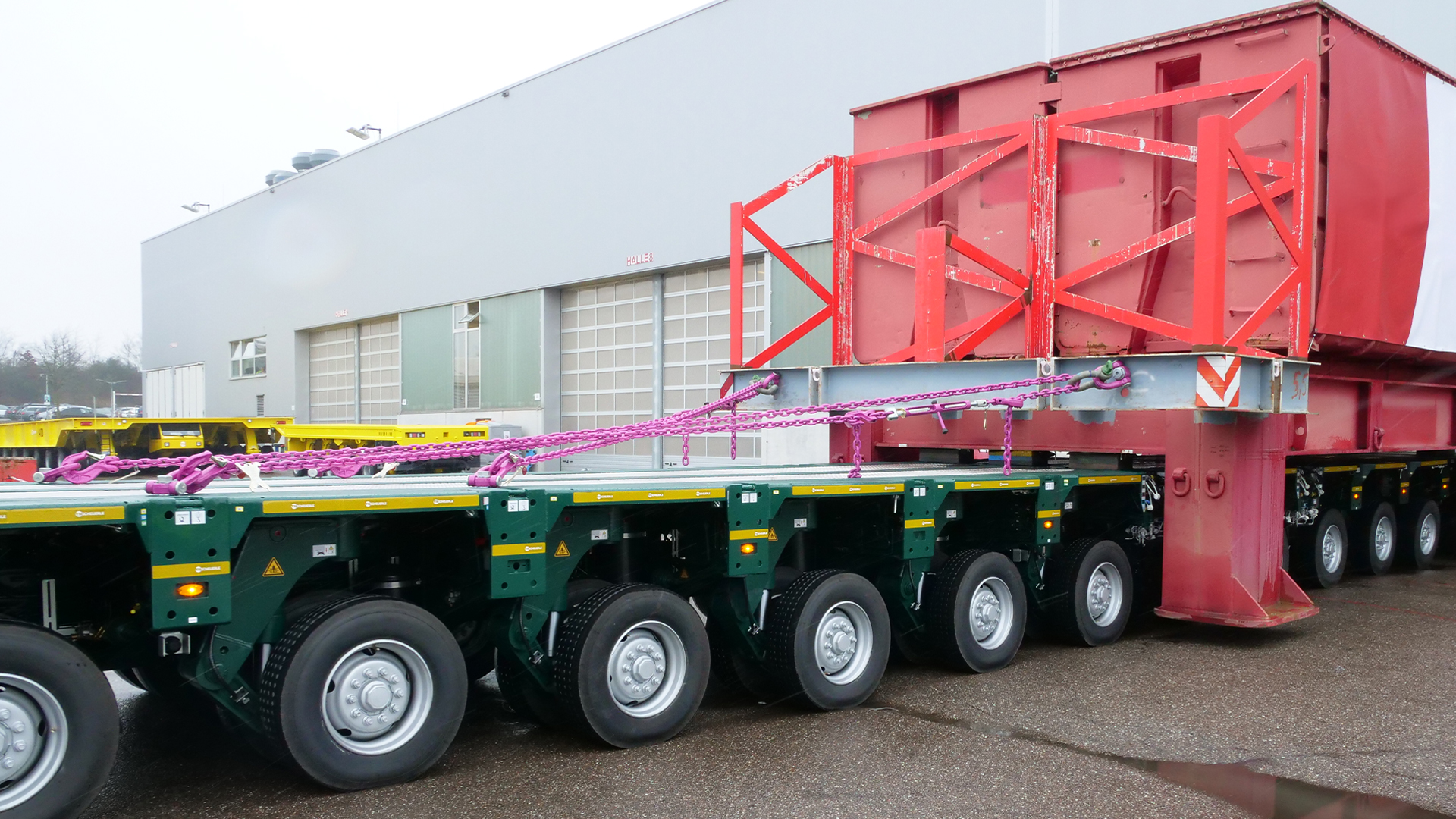 Schwerlasttransport mit Anhänger, auf dem eine große Struktur mit pinkfarbenen Ketten gesichert ist.