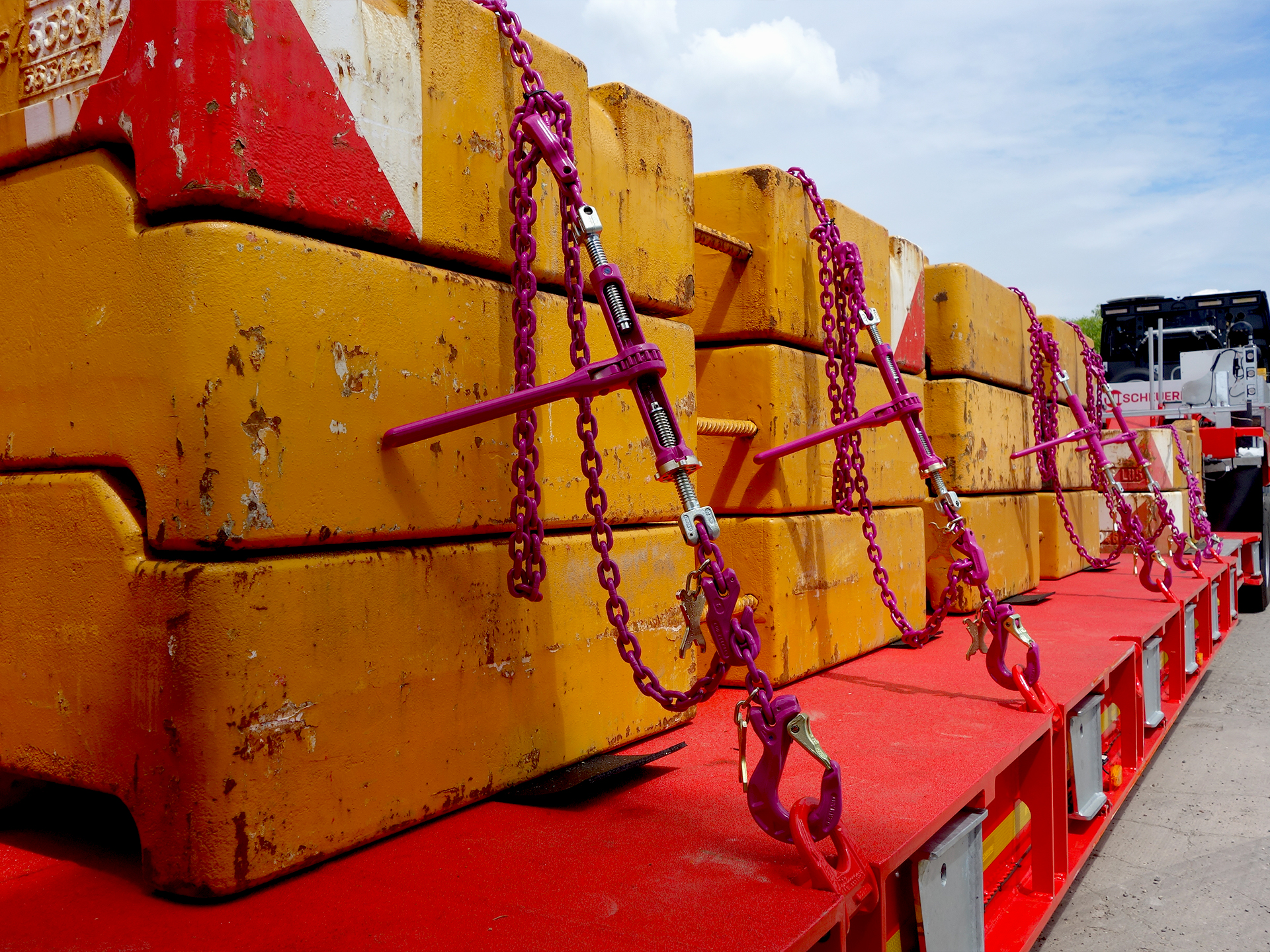 Gelbe Beton-Gegengewichte auf einem Tieflader mit RUD-Zurrketten in Pink gesichert.