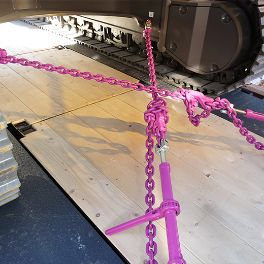 Schweres Gerät über Kreuz auf Holzplattform festgezurrt