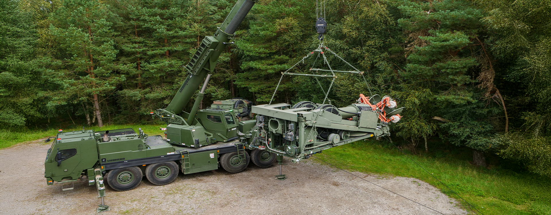 Militärkran hebt ein schweres Systemmodul mit RUD Anschlagsystemen in einem Waldgebiet an.