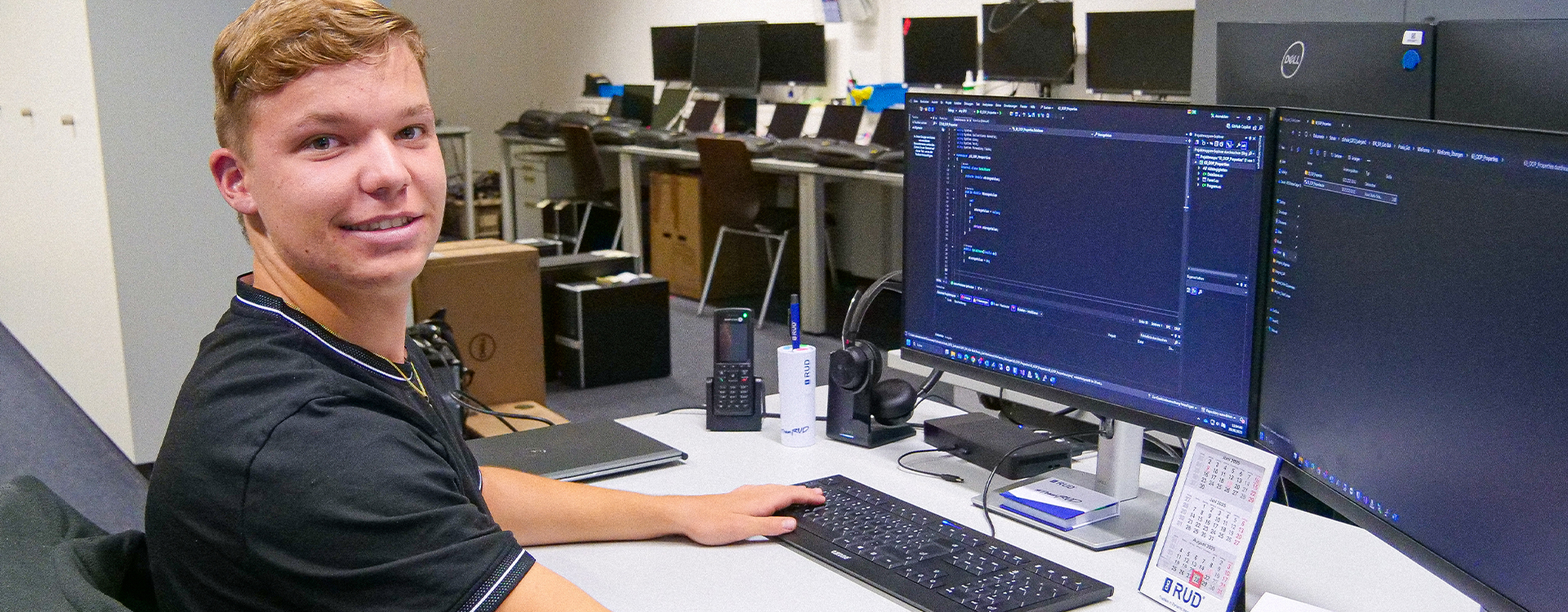 Auszubildender Fachinformatiker bei RUD programmiert an zwei Monitoren im Büro.
