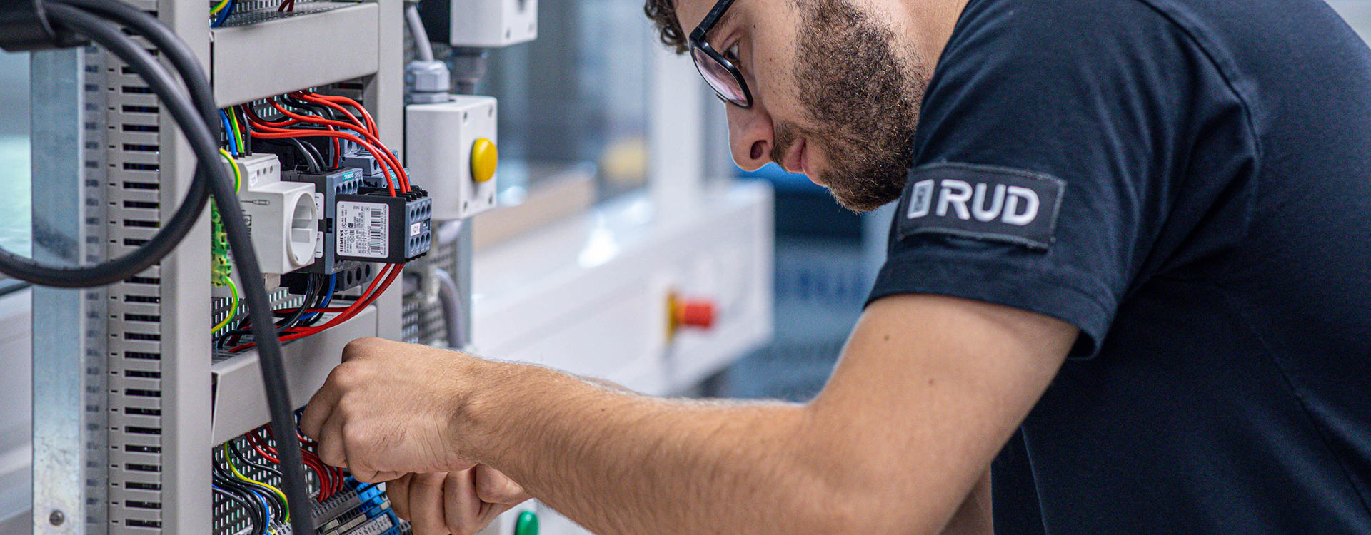 Ein Elektroniker arbeitet konzentriert an der Verkabelung eines offenen Schaltschrankes.