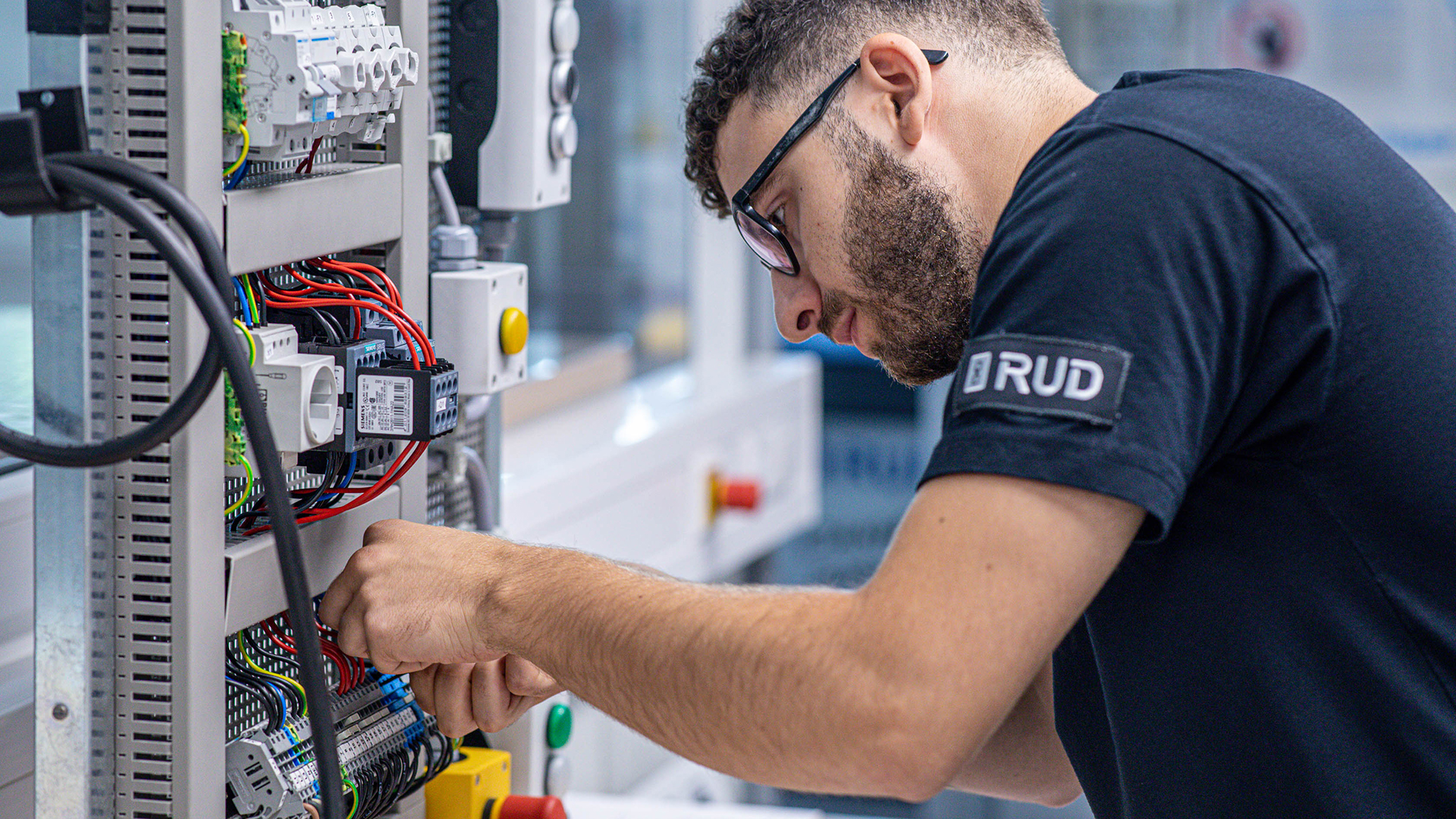 Ein Elektroniker arbeitet konzentriert an der Verkabelung eines offenen Schaltschrankes.