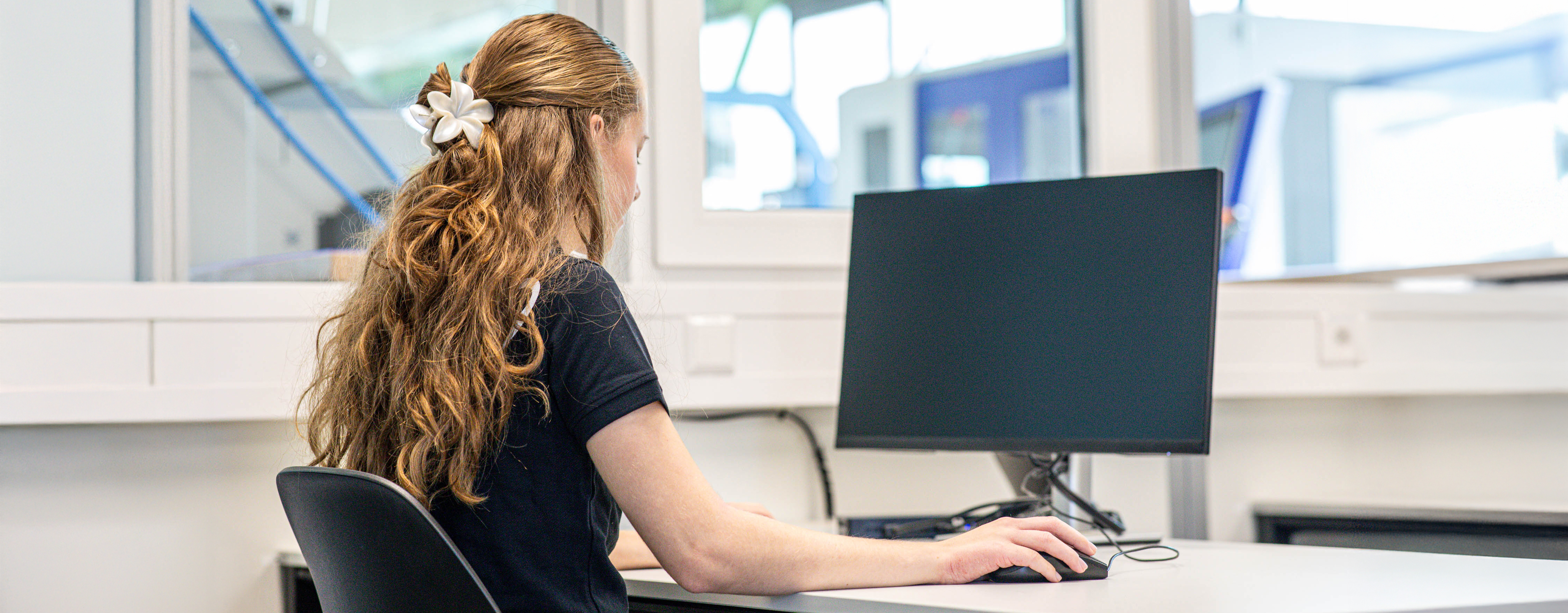 Eine junge RUD Mitarbeiterin sitzt im Büro an einem Schreibtisch und arbeitet konzentriert am Computer.
