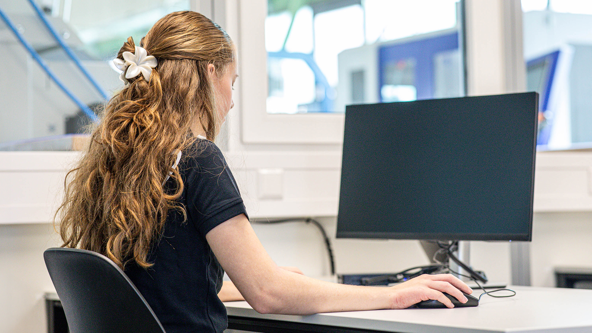 Eine junge RUD Mitarbeiterin sitzt im Büro an einem Schreibtisch und arbeitet konzentriert am Computer.