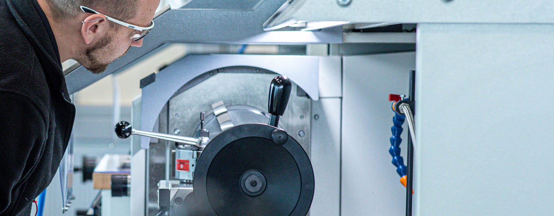 Ein RUD Mitarbeiter mit Schutzbrille betrachtet konzentriert eine Drehmaschine in einer Werkhalle.
