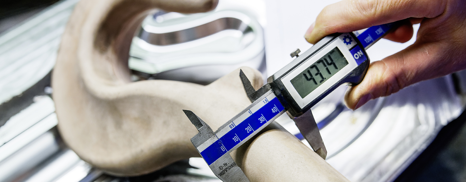 Eine Person misst ein Werkstück mit einer digitalen Schieblehre, die 43,74 mm anzeigt.