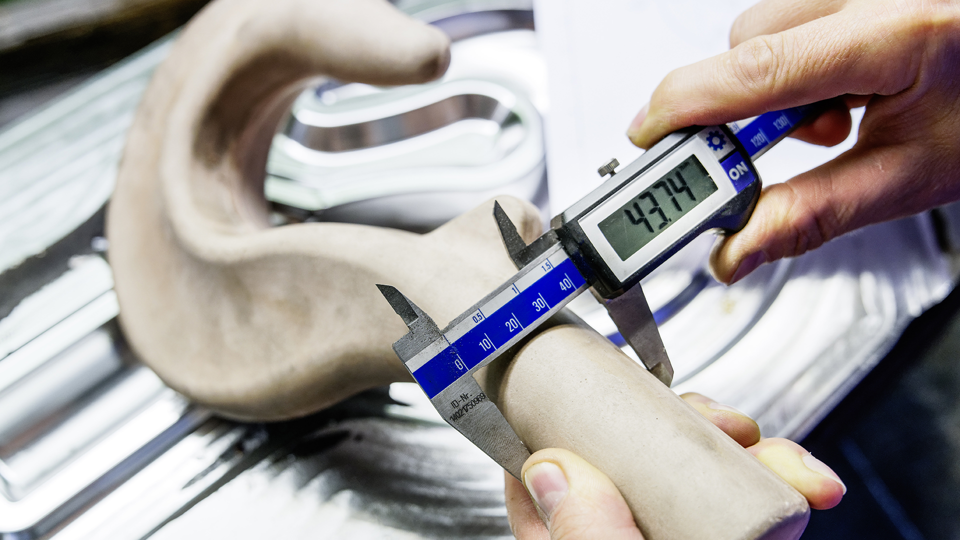 Eine Person misst ein Werkstück mit einer digitalen Schieblehre, die 43,74 mm anzeigt.