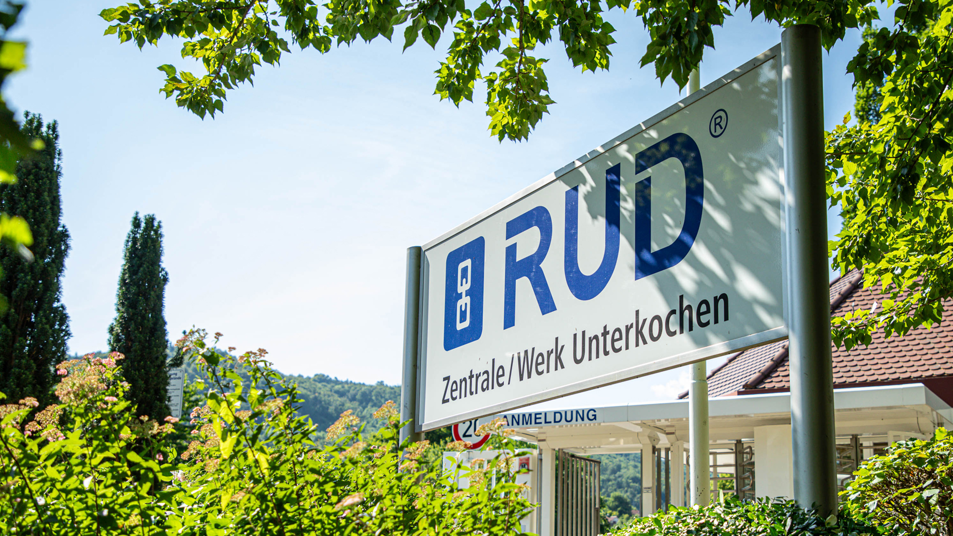 Eingangsschild am Eingangsbereich des RUD Firmenstandorts in Aalen-Unterkochen, umgeben von Grünpflanzen und Bäumen.