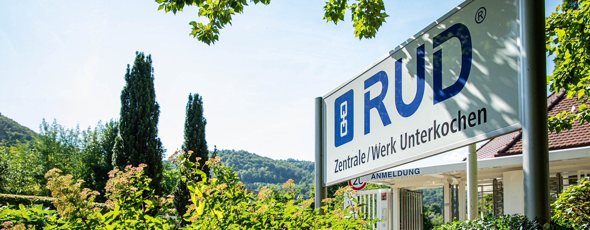 Eingangsschild am Eingangsbereich des RUD Firmenstandorts in Aalen-Unterkochen, umgeben von Grünpflanzen und Bäumen.