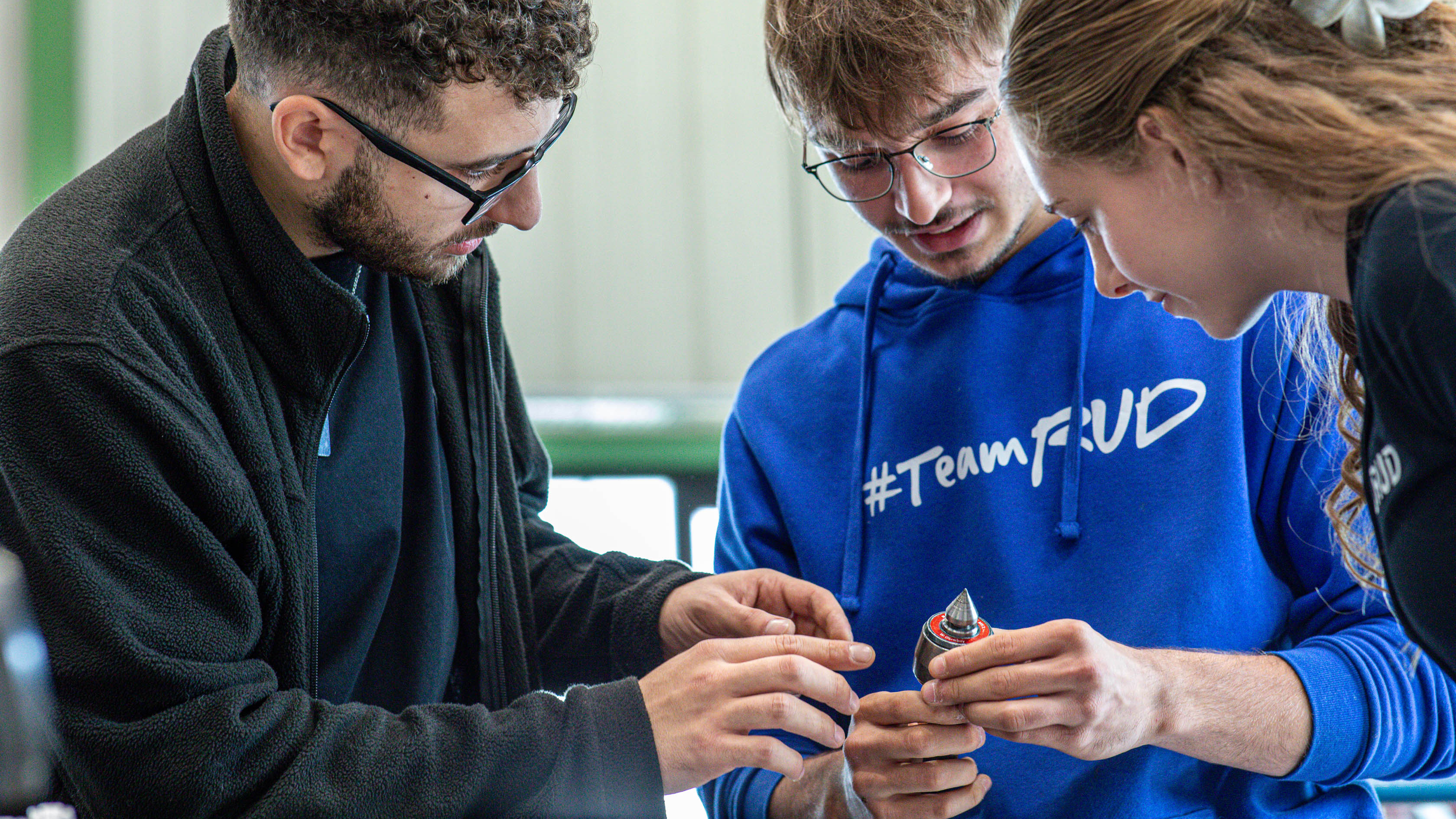 Drei RUD Werkstudenten betrachten gemeinsam ein metallisches Bauteil und besprechen dessen Details.