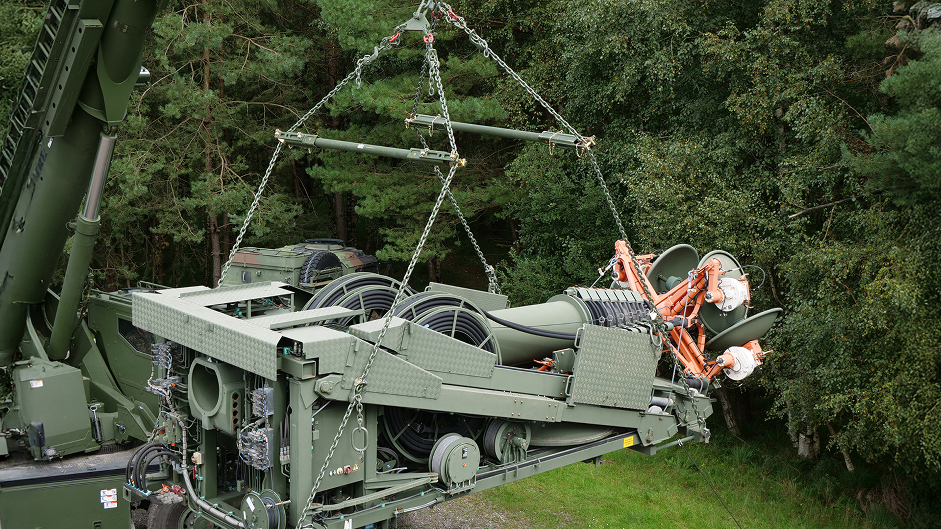 Militärisches Spezialgerät mit RUD-Hebesystem wird im Gelände per Kran gehoben, umgeben von Wald.