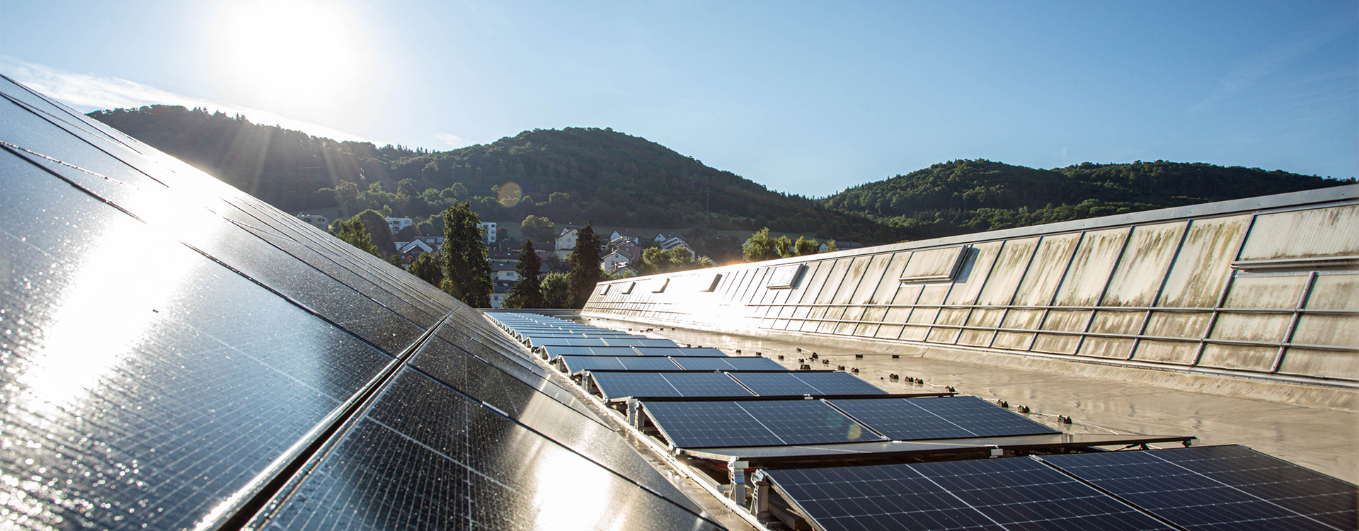Solaranlage auf dem Dach eines RUD-Gebäudes mit Blick auf bewaldete Hügel im Sonnenlicht.