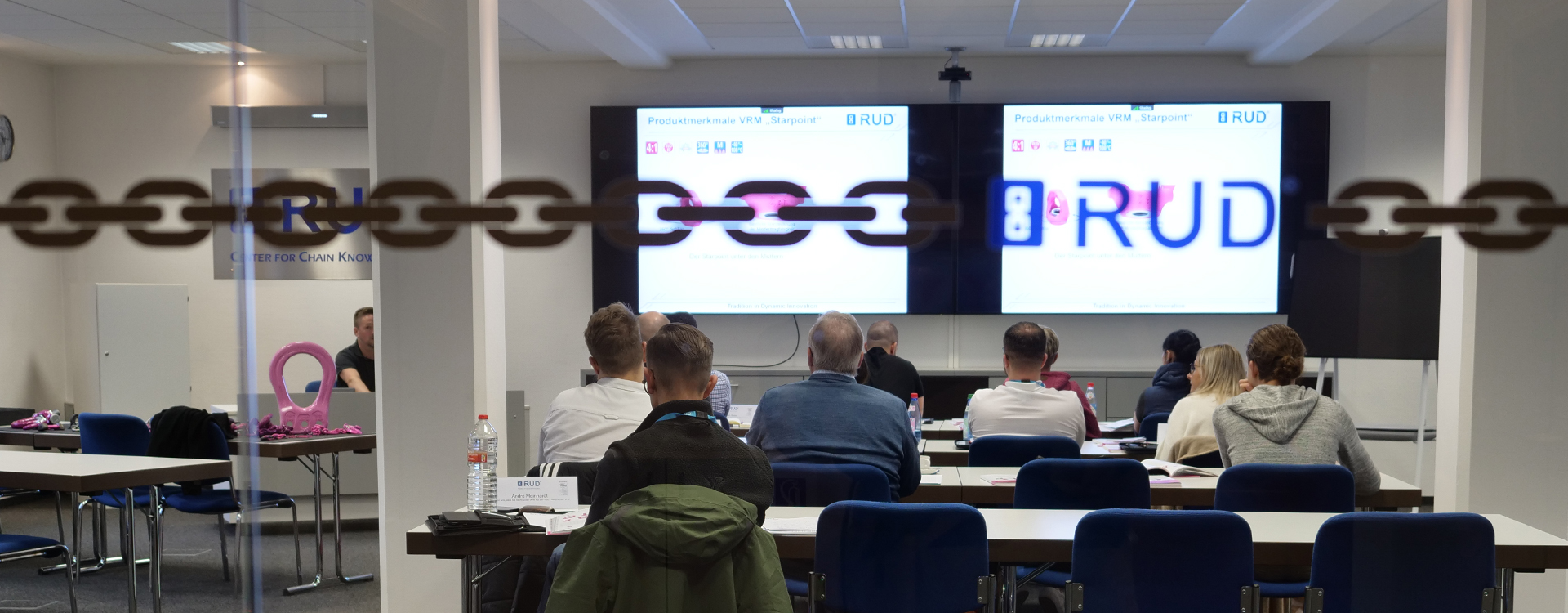 Teilnehmer in einem RUD-Schulungsraum verfolgen eine Präsentation zu Produktmerkmalen auf großen Bildschirmen.